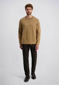 Pull marron clair avec un col rond, texture tricotée, associé à un pantalon noir marron ajusté et des chaussures en cuir marron.