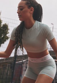 Lys blå atletisk crop top og matchende shorts med rosa "Jordan" midjebånd. Glatt tekstur, tettsittende design og subtile merkevareakenter.