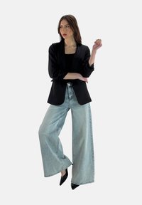 Blazer nero con rever strutturati, abbinato a jeans a gamba larga azzurri e décolleté nere a punta. Texture liscia, design minimalista.
