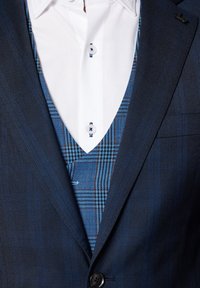 Granatowa marynarka z niebieską kraciastą kamizelką pod spodem. Biała koszula z niebieskimi guzikami. Teksturowany materiał z gładkim wykończeniem.
