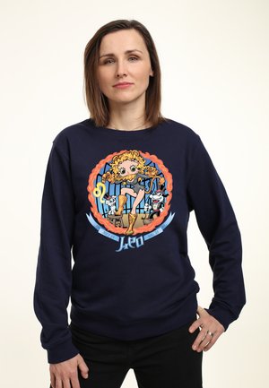 Marine sweatshirt med et levende tegneseriegraphic af en dansende karakter rammet af flammer, med legende accenter og et blåt bånd nedenfor.