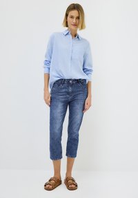 Modrá a bílá pruhovaná košile na knoflíky, džíny typu capri z denimu a hnědé sandály se cvočky. Úzký střih, měkký materiál, neformální design.