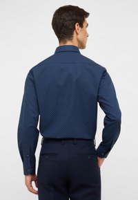 Camicia blu navy con bottoni, caratterizzata da un motivo a pois bianchi, maniche lunghe e colletto classico, realizzata in tessuto liscio.