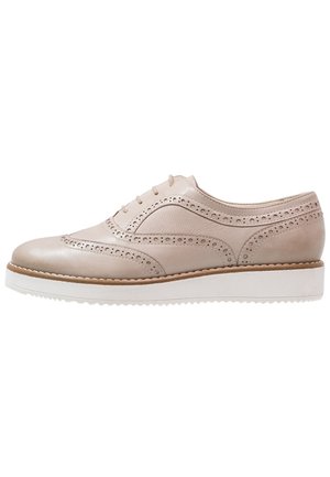 Beige læder brogue sko med perforerede detaljer, snørelukning og hvid gummisål med rillede bund.