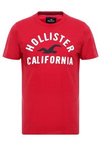 Punainen puuvillapaita, jossa on pyöreä kaula-aukko, lyhyet hihat ja "HOLLISTER CALIFORNIA" -teksti valkoisena mustalla korostettuna linnugrafiikalla.