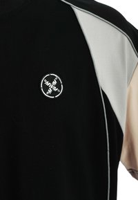 Camiseta negra de manga corta, con acentos grises y un logo redondo bordado en la parte frontal. Material de algodón suave.