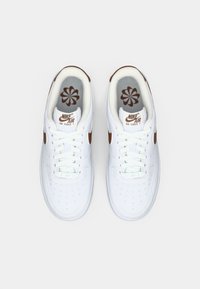 Bijele Nike Air Force 1 tenisice s smešnim Swoosh-om i logotipom, viđene odozgo na ravnoj bijeloj pozadini.