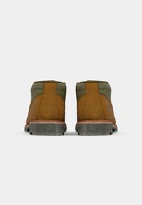Bottines en cuir marron et textile vert avec une semelle en caoutchouc, dotées d'un col rembourré et de détails en tan contrastants sur le talon.