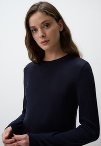 Maglione blu navy realizzato in tessuto a maglia, con scollatura rotonda e maniche lunghe a vestibilità rilassata, esposto su uno sfondo bianco.