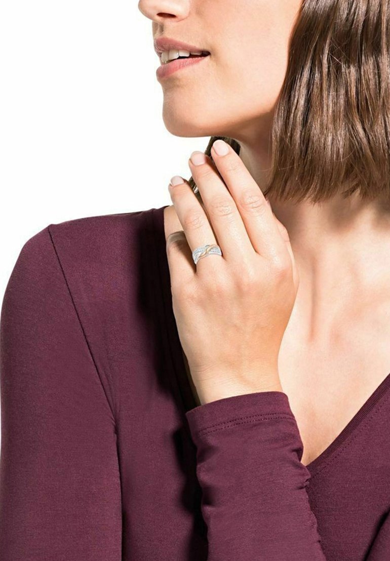 Anello d'argento con design intrecciato, dotato di piccole pietre trasparenti. Il modello ha capelli di lunghezza media e indossa un top a maniche lunghe color bordeaux.