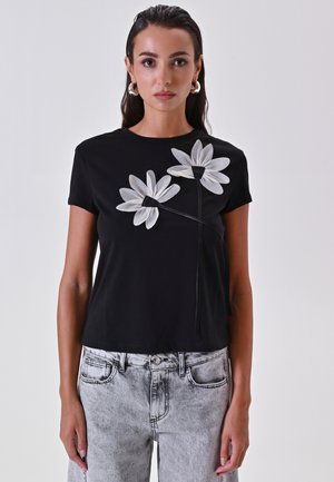 Schwarzes Baumwoll-T-Shirt mit großer weißer Blumenstickerei auf der Vorderseite. Kurze Ärmel, runder Halsausschnitt und lockerer Schnitt.