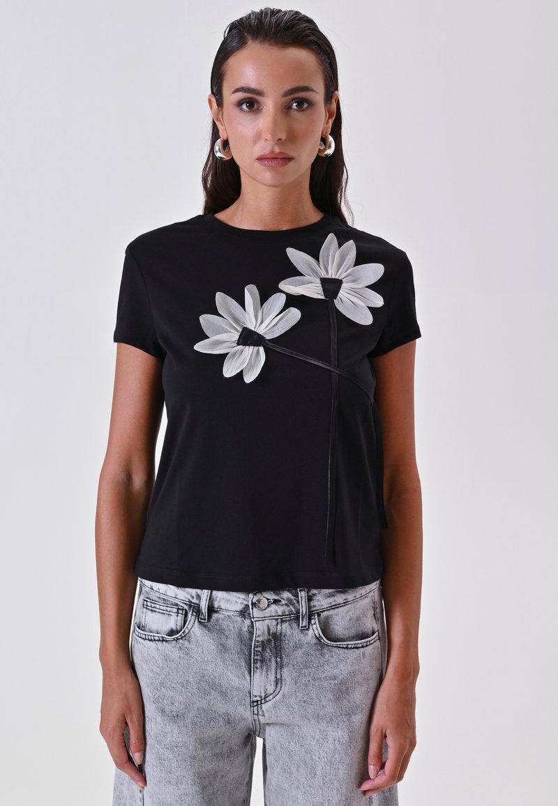 Zwarte katoenen T-shirt met grote witte bloemenborduring op de voorkant. Korte mouwen, ronde halslijn en een relaxte pasvorm.