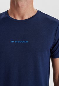 Marineblå bomulds t-shirt med rund halsudskæring, der har teksten "JBS OF DENMARK" i lyseblå på brystet.