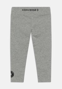 Szürke stretch leggings, amelyek puha anyagból készültek, testhezálló kialakításúak, elasztikus derékkal, rajta "CONVERSE" felirattal és egy kör alakú logóval a lábon.
