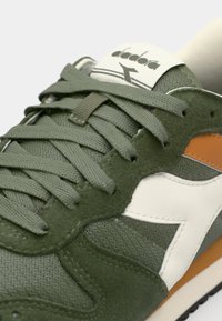 Green athletic shoes with a textured suede and mesh upper, white logo detail, gray laces, and orange accents near the sole.