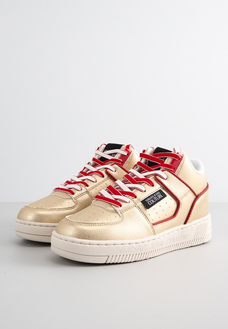Sneaker alte con una finitura metallica dorata, lacci rossi e dettagli neri. Caratterizzate da perforazioni e una suola bianca testurizzata.
