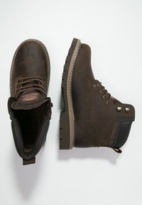 Botas de tobillo de cuero marrón con un acabado texturizado, puntera reforzada y suela de goma con profundos relieve y detalles metálicos.