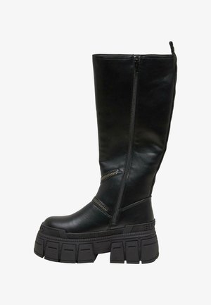 Czarne, sięgające za kolano botki, wykonane z gładkiej skóry, z masywną platformą i wieloma zamkami błyskawicznymi po zewnętrznej stronie. Teksturowana gumowa podeszwa.