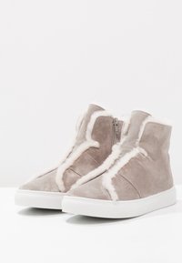Szare zamszowe sneakersy typu high-top z białym sztucznym futerkiem w środku, gładką fakturą i zamkiem błyskawicznym z boku. Gumowa podeszwa z teksturowanym wykończeniem.