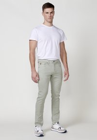 Jeans ajustados de color verde claro con una textura suave, combinados con una camiseta blanca lisa y zapatillas deportivas grises. Diseño sencillo y mínimos detalles.