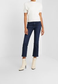 Top blanco de punto con relieve y mangas cortas abullonadas, combinado con vaqueros recortados oscuros y botas de tobillo crema con punta y tacón alto.