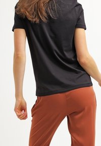 Camisa negra de manga corta con textura suave, combinada con pantalones de color óxido. Enfocada en líneas limpias y un diseño simple.