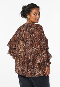Brown snake-print blouse with layered ruffle sleeves, featuring a textured fabric and relaxed fit. Worn over black pants.