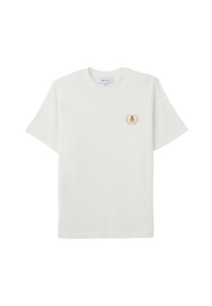 Camiseta de algodón blanca con mangas cortas, que presenta un pequeño emblema de un oso en dorado y marrón dentro de un diseño de laurel en el lado izquierdo del pecho.