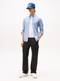 Lichtblauwe button-down shirt, witte t-shirt, zwarte cargo broek en witte sneakers. Blauwe pet met geborduurde tekst en een ontspannen pasvorm.
