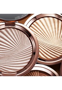Highlighterkompakta i roséguldfodral med präglade vågmönster. Nyansena inkluderar silver, guld och bronstoner. Släta metalliska ytor.