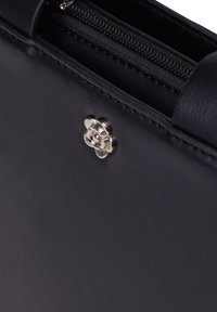Borsa in pelle nera con una texture liscia, dotata di un accento hardware floreale in argento e una cerniera lungo il bordo superiore.