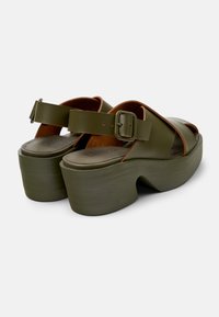 Olivgröna platåsandaler med justerbar rem och spänne, med en slät yta, böjd klack och mjukt brun innertyg.