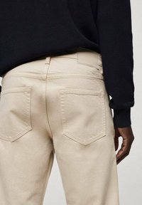 Jeans de mezclilla beige con un corte relajado, que cuentan con dos bolsillos traseros, detalles de costura sutiles y una cintura de tejido medio.