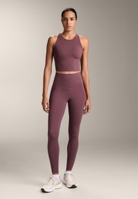 Bordový športový crop top a legíny s vysokým pásom, hladká textúra, elegantný dizajn, kombinované s bielymi atletickými topánkami. Minimalistický štýl.