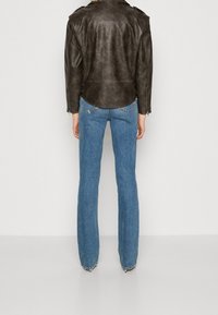 Veste en cuir marron au design ajusté avec épaulettes, associée à un jean flare bleu au coupe classique avec un ourlet légèrement effiloché.