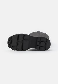 Zwarte rubberen laarszool met een gestructureerd oppervlak, voorzien van uitgesproken groeven en een afgeronde neus voor verbeterde grip en duurzaamheid.