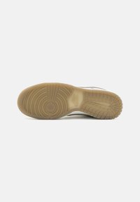 Podešev boty z béžové gumy s texturovaným vzorem obsahujícím kruhové drážky a horizontální linie, navržená pro zajištění trakce a odolnosti.