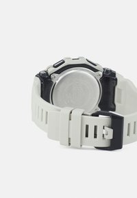 Montre en caoutchouc gris avec une lunette noire, un bracelet texturé et un fermoir en métal. L'arrière présente une finition argentée avec des marquages en relief.