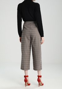Šedé kostkované vysoké kalhoty culottes s širokým střihem nohavic, spárované s červenými sandály na vysokém podpatku se zpruhovanými popruhy. Černé dlouhé rukávy dokončují celkový vzhled.