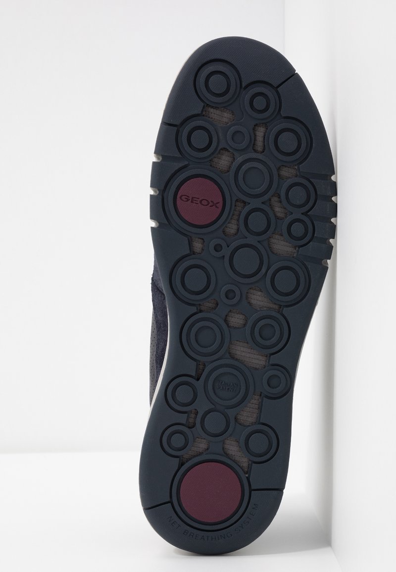 Semelle de chaussure bleu marine foncé avec des motifs de traction circulaires, comportant des accents en caoutchouc surélevés et le logo "GEOX" en rouge. Design texturé et respirant.