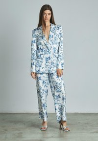 Completo floreale in satin bianco con fiori blu. Include un blazer con revers e pantaloni a gamba larga. Completato con sandali con tacco alto argento.