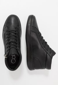 Baskets montantes en cuir noir avec un design à lacets, fermeture éclair, texture lisse et semelle en caoutchouc contrastée. Pas de logos ni de motifs visibles.