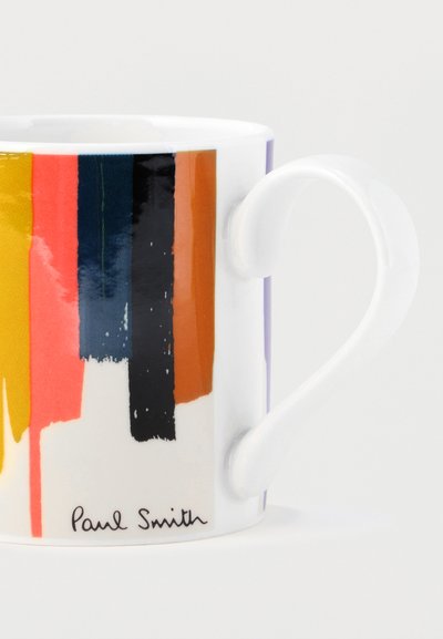 Tasse en céramique blanche avec des rayures abstraites verticales en coups de pinceau jaune, corail, marine, noir et marron, signée « Paul Smith » en bas.