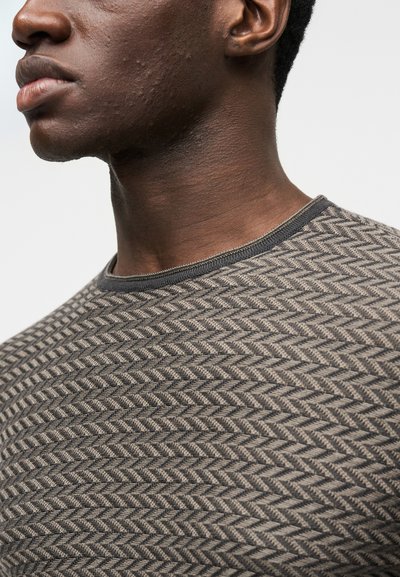 Camisola com padrão espinha de peixe em tons castanhos com acabamento preto na gola. Feita em tecido de malha texturizado. Vista de perto do decote e do ombro.