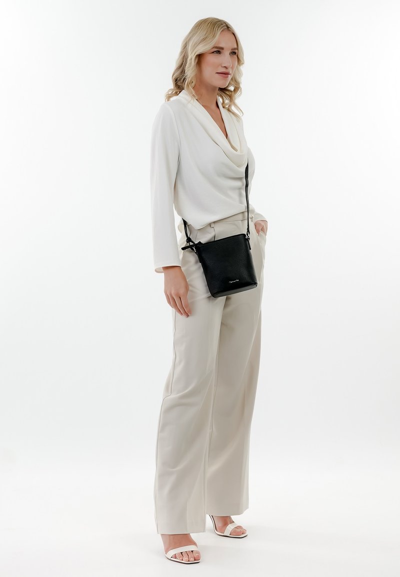 Bolso bandolera negro con textura de grano, acentuado por correas ajustables, combinado con una blusa blanca drapeada y pantalones de pierna ancha color crema.