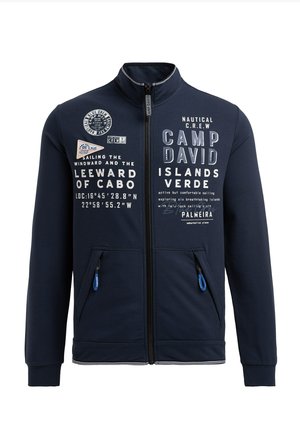 Marineblaue Jacke mit Reißverschluss und hohem Kragen, mit weißem Text und nautischen Grafiken. Verfügt über zwei Fronttaschen mit blauen Reißverschlussanhängern.