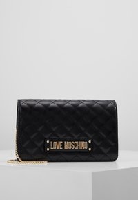 Borsa trapuntata nera realizzata in materiale lucido, con una placca logo dorata e una tracolla a catena. Design compatto con chiusura a battente.