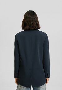 Mörk marinblå blazer med en jämn textur, enkel bakventil, notchade slag och långa ärmar, i kombination med ljusa denimbyxor.