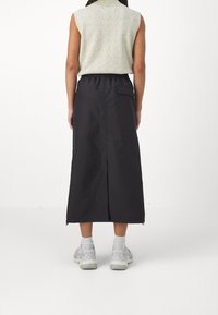 Musta pitkä hame, joka on valmistettu sileästä kankaasta. Hameessa on joustava vyötärö, takatasku ja halkio helman kohdalla. Se on yhdistetty vaaleanvihreään toppiin.