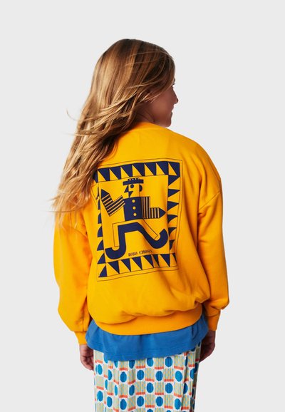 Felpa gialla con un design grafico blu sul retro che presenta una figura stilizzata, motivi geometrici e una vestibilità comoda.